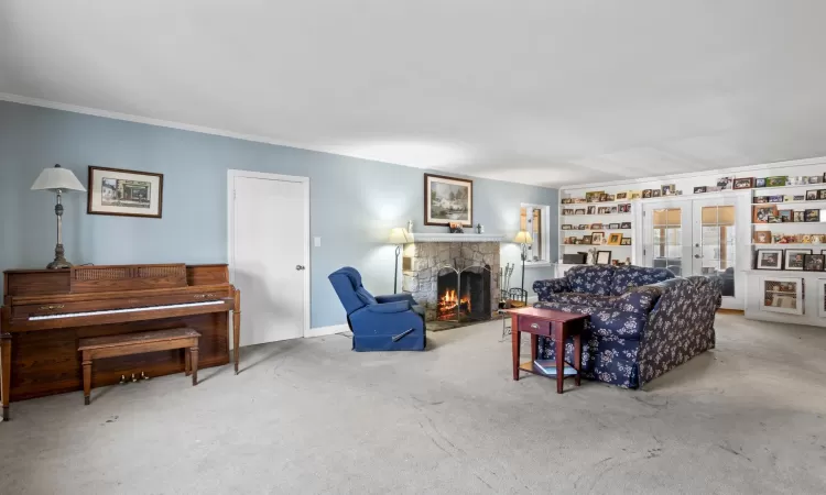 Carpeted living room with ornamental molding, french doors, and a stone fireplace