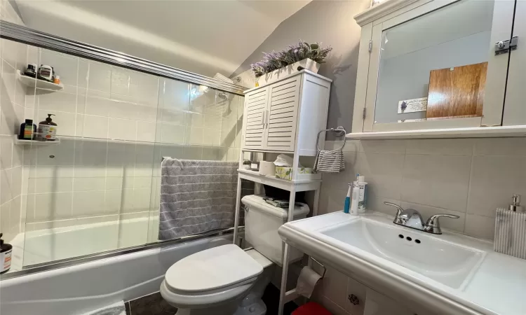 Full bathroom with lofted ceiling, sink, backsplash, toilet, and combined bath / shower with glass door