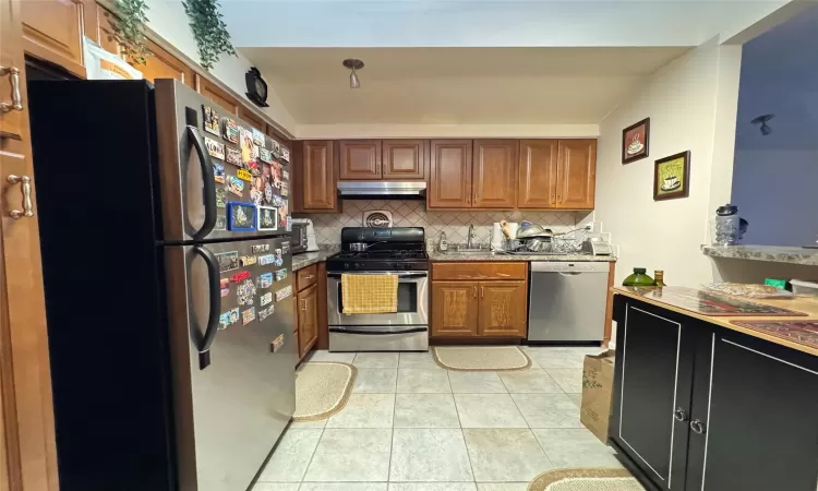 Kitchen with tasteful backsplash, light tile patterned floors, and appliances with stainless steel finishes