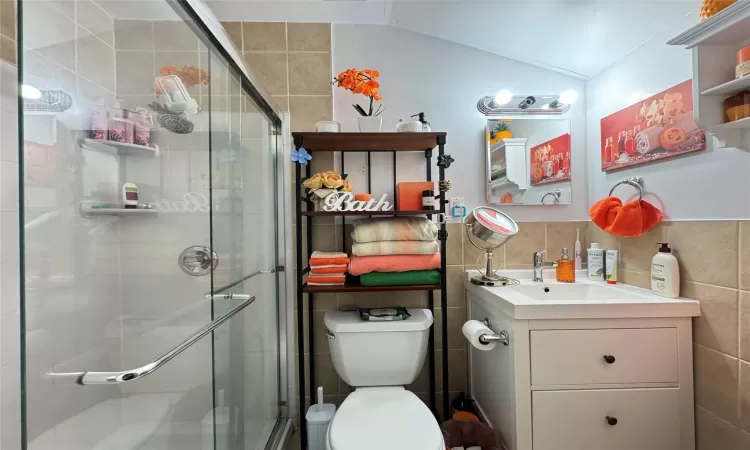 Bathroom featuring walk in shower, vanity, vaulted ceiling, backsplash, and toilet