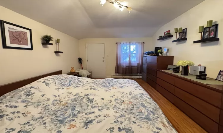 Bedroom featuring baseboard heating, lofted ceiling, and hardwood / wood-style flooring