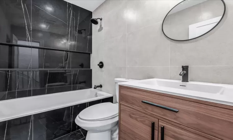 Full bathroom featuring tile walls, tiled shower / bath combo, vanity, and toilet