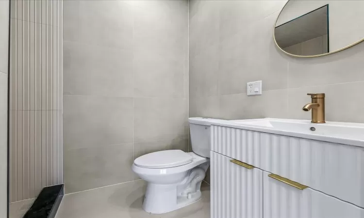 Bathroom featuring toilet, vanity, and tile walls