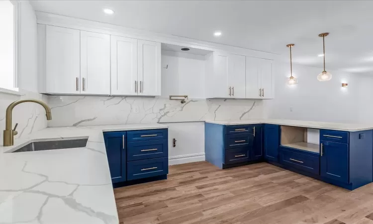 Kitchen featuring white cabinets, sink, blue cabinetry, and pendant lighting