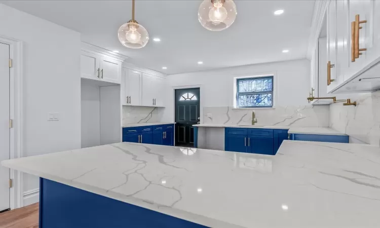 Kitchen with backsplash, light stone countertops, pendant lighting, white cabinets, and sink