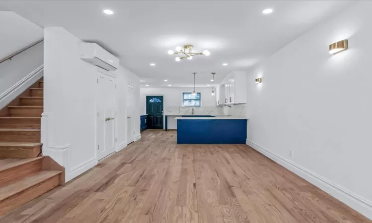 Kitchen with an AC wall unit, white cabinets, decorative backsplash, hanging light fixtures, and light wood-type flooring