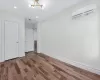 Unfurnished bedroom with a wall mounted AC, a notable chandelier, and hardwood / wood-style flooring