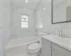 Full bathroom with toilet, tile walls, vanity, and tiled shower / bath combo