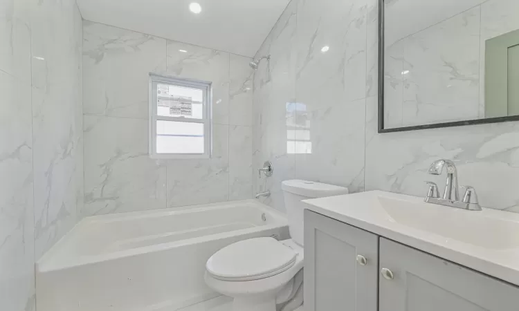 Full bathroom with toilet, tile walls, vanity, and tiled shower / bath combo