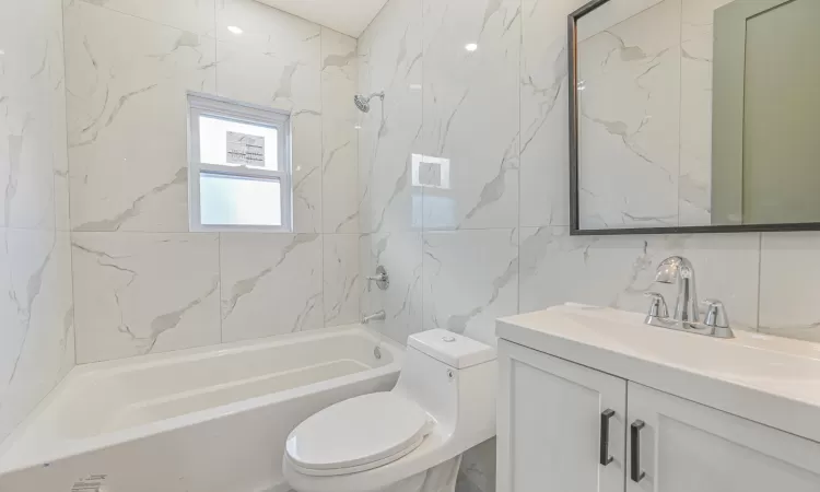 Full bathroom with toilet, tiled shower / bath, tile walls, vanity, and decorative backsplash