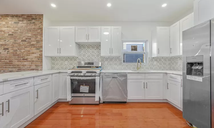 Kitchen with white cabinetry, appliances with stainless steel finishes, backsplash, light wood-type flooring, and sink