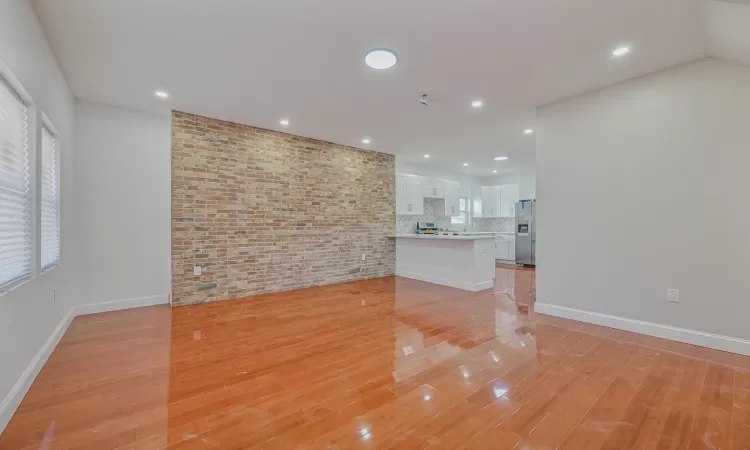 Unfurnished living room with brick wall and light wood-type flooring