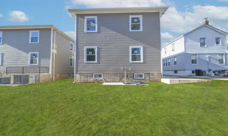 Back of house with central AC unit and a lawn