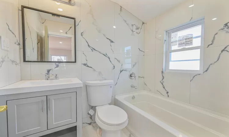 Full bathroom featuring toilet, tiled shower / bath combo, vanity, and tile walls