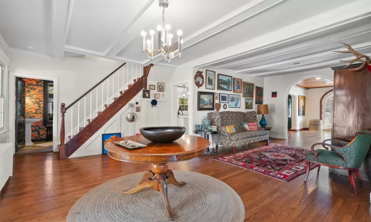 Living room featuring hardwood flooring, beamed ceiling, an inviting chandelier, and ornamental molding