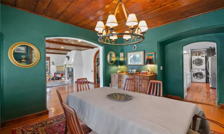 Dining area with a fireplace, hardwood / wood-style flooring, stacked washer and clothes dryer, a chandelier, and wooden ceiling