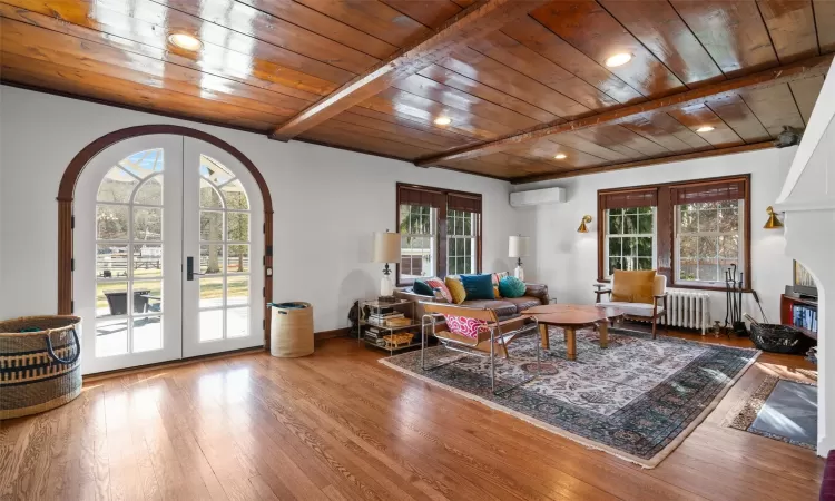 Living room featuring wooden ceiling, a wall mounted AC, beam ceiling, and radiator heating unit