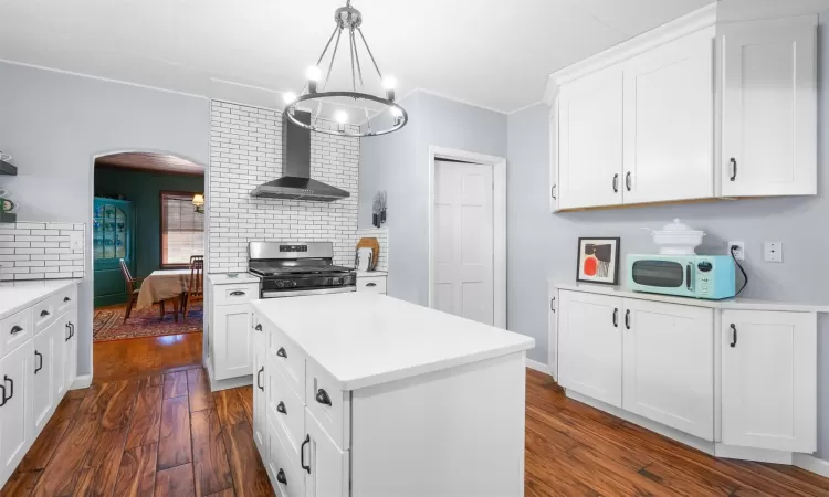 Kitchen featuring white cabinetry, stainless steel gas range oven, backsplash, decorative light fixtures, and wall chimney range hood