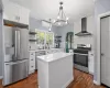 Kitchen featuring appliances with stainless steel finishes, a center island, wall chimney exhaust hood, white cabinetry, and backsplash