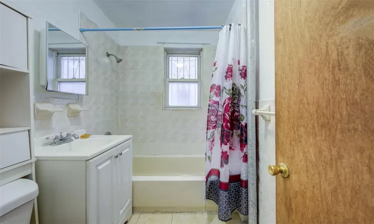 Full bathroom featuring toilet, shower / bath combo with shower curtain, tile patterned flooring, tile walls, and vanity