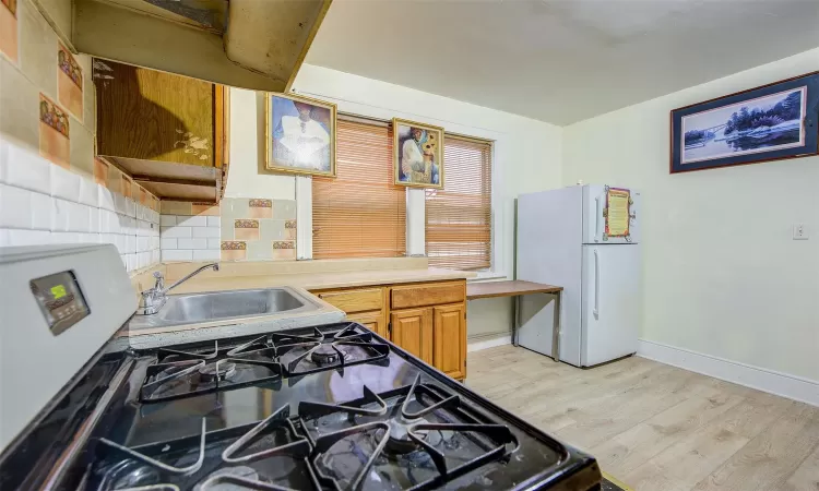 Kitchen featuring backsplash, gas stove, light hardwood / wood-style floors, sink, and white refrigerator