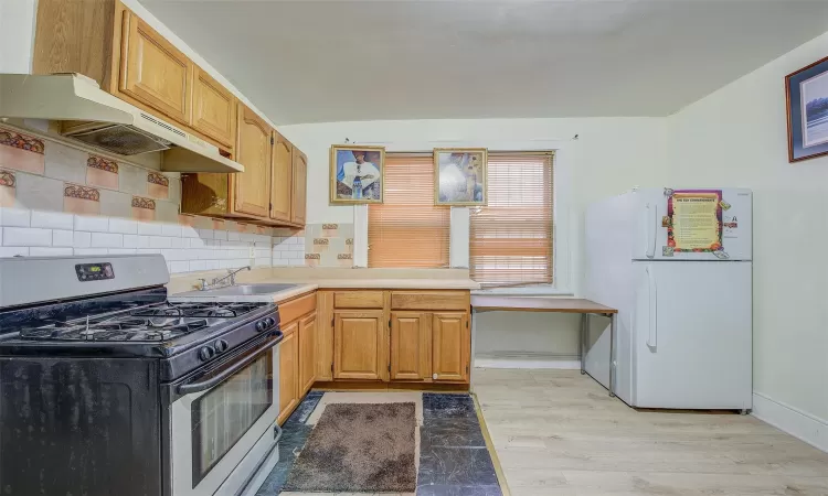 Kitchen featuring white fridge, sink, backsplash, light wood-type flooring, and gas range