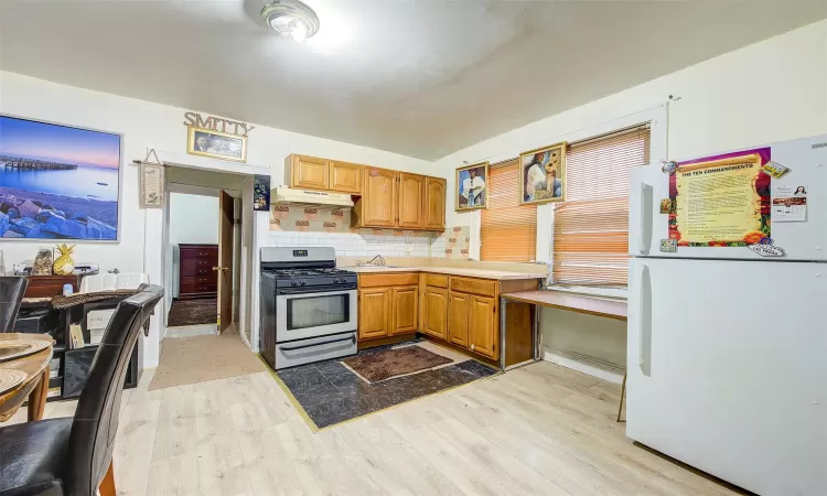 Kitchen featuring white refrigerator, decorative backsplash, sink, stainless steel range with gas cooktop, and light hardwood / wood-style flooring