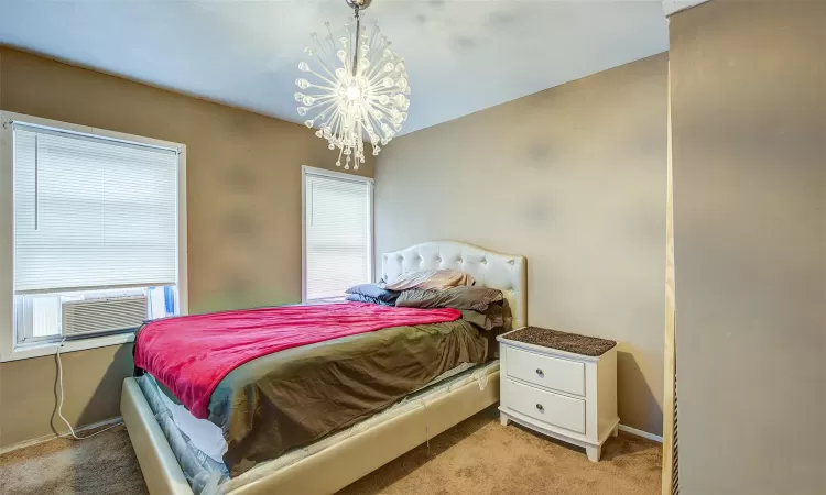 Bedroom with light colored carpet, multiple windows, cooling unit, and an inviting chandelier