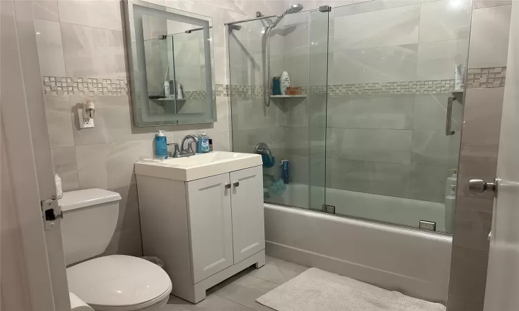 Full bathroom with toilet, combined bath / shower with glass door, tile patterned flooring, tile walls, and vanity