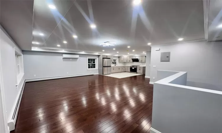 Unfurnished living room featuring baseboard heating, dark hardwood / wood-style flooring, an AC wall unit, and electric panel