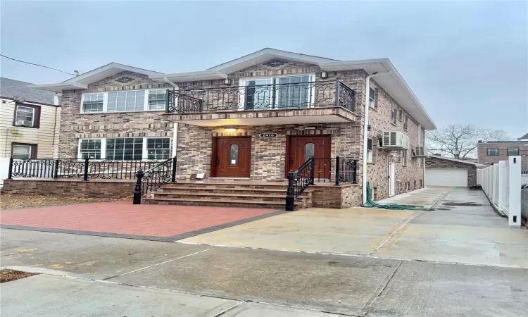 View of front facade with a garage, a wall mounted AC, an outbuilding, and a balcony