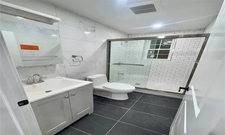 Bathroom featuring an enclosed shower, tile patterned floors, vanity, tile walls, and toilet