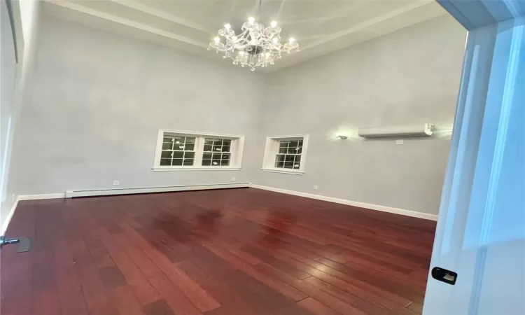 Spare room with a baseboard heating unit, a chandelier, a wall mounted AC, and hardwood / wood-style flooring