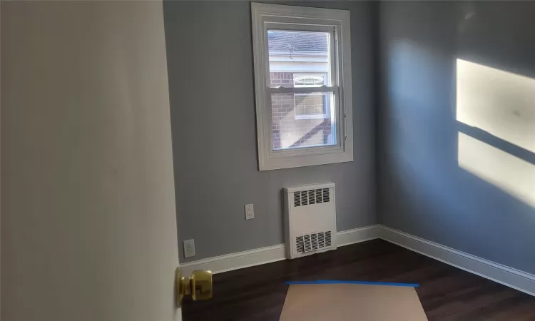 Empty room with dark hardwood / wood-style floors and radiator