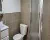 Bathroom with toilet, vanity, tile walls, and a shower with door