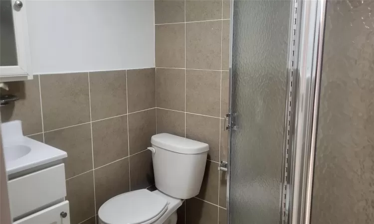 Bathroom with toilet, vanity, tile walls, and a shower with door