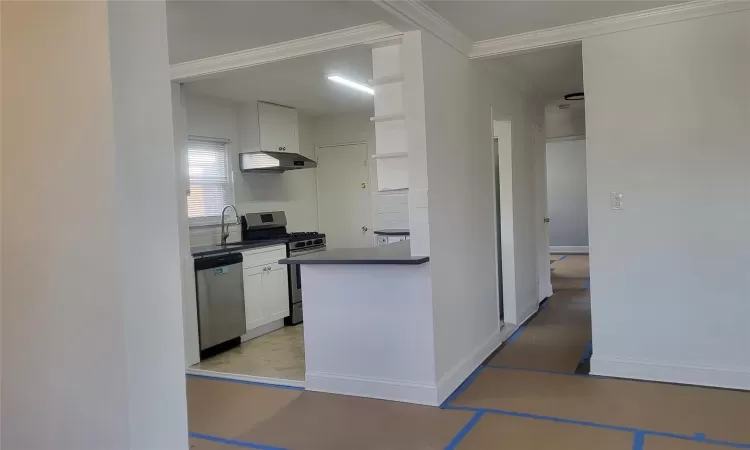 Kitchen with appliances with stainless steel finishes, ornamental molding, and white cabinets