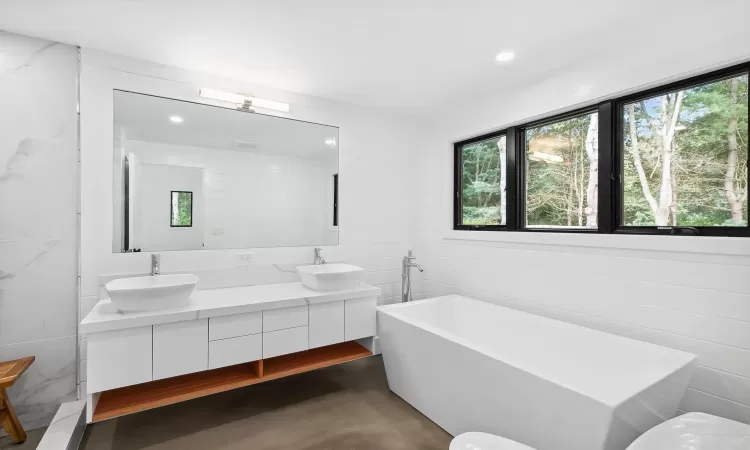 Bathroom with concrete flooring, a tub to relax in, and vanity