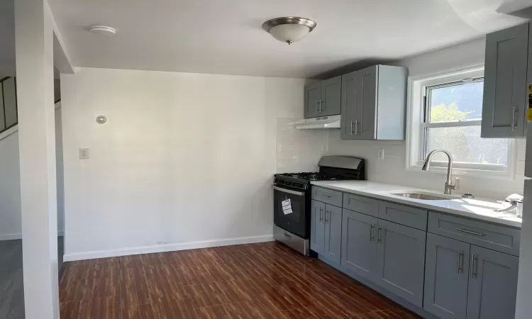 Kitchen with gray cabinets, decorative backsplash, stainless steel range with gas stovetop, and sink