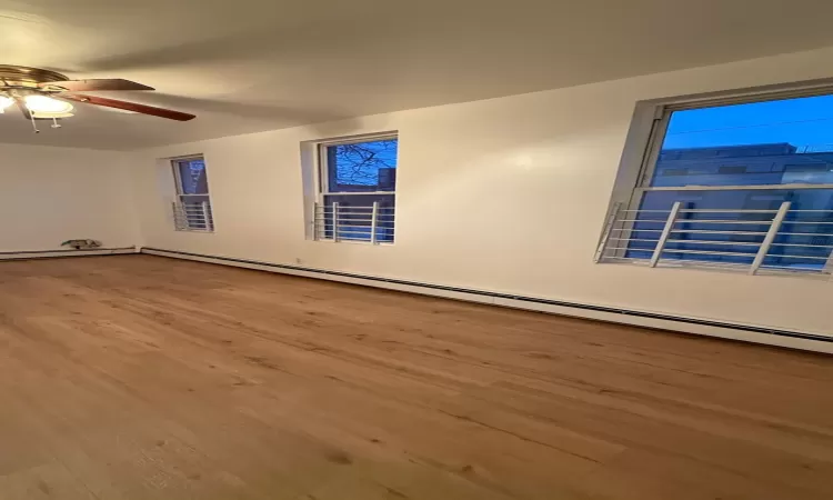 Unfurnished room featuring ceiling fan, hardwood / wood-style floors, and a baseboard heating unit