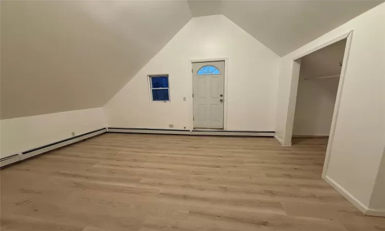 Foyer entrance with light hardwood / wood-style floors, baseboard heating, and lofted ceiling