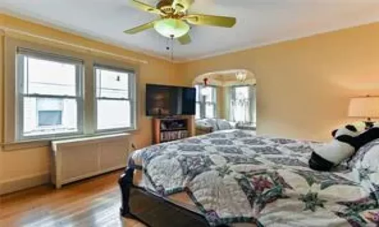 Bedroom featuring ceiling fan, wood-type flooring, and crown molding