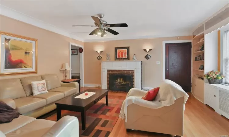 Living room featuring ceiling fan, light wood-type flooring, a fireplace, and crown molding