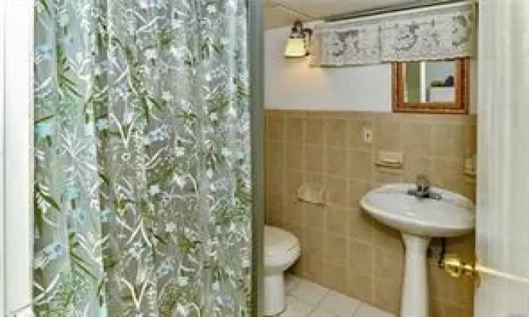 Bathroom with toilet, tile walls, tile patterned flooring, and a shower with curtain