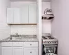 Kitchen with sink, white range with electric cooktop, backsplash, and white cabinetry