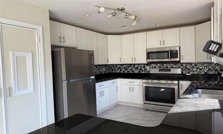 Kitchen featuring stainless steel appliances, decorative backsplash, white cabinets, and dark stone counters