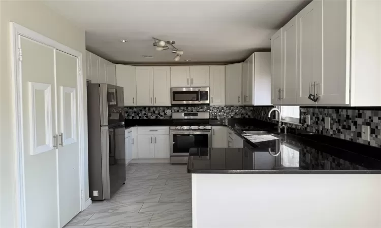 Kitchen featuring appliances with stainless steel finishes, white cabinetry, decorative backsplash, sink, and kitchen peninsula