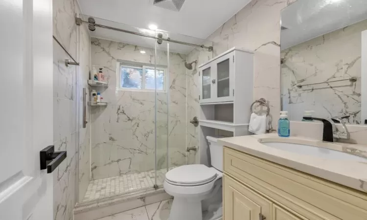 Bathroom featuring vanity, a shower with shower door, and toilet