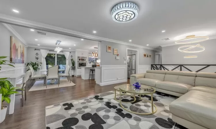 Living room featuring dark wood-type flooring, crown molding, and a notable chandelier