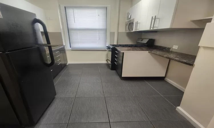 Kitchen featuring appliances with stainless steel finishes, white cabinetry, dark stone counters, and dark tile patterned floors